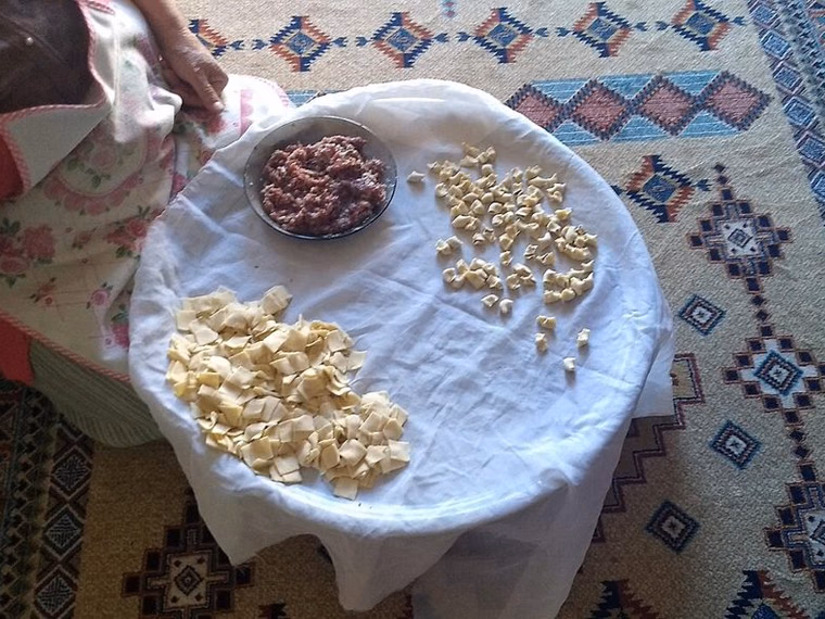 Kayseri mantı being made at home: dough squares, a bowl of minced meat and tiny folded mantı on a cloth