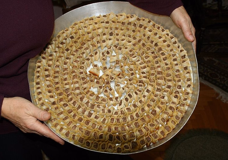 Tray of open-topped mantı arranged in a spiral before baking