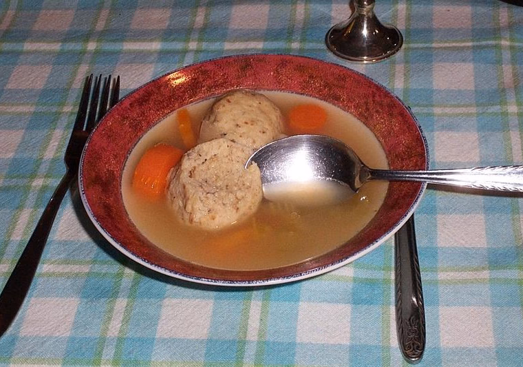 Matzah balls in chicken soup with carrots, bowl on a checked tablecloth. Round, cooked.
