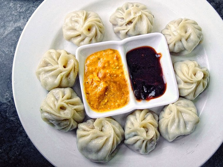 Plate of steamed momo with two dipping sauces; round purse fold with spiral pleats. Cooked.
