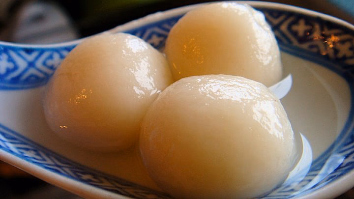 Three homemade white tangyuan in a blue-and-white bowl; smooth round unfilled-look surface. Cooked.